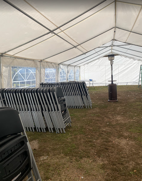 Inside view of a white frame tent with stacked chairs and heater