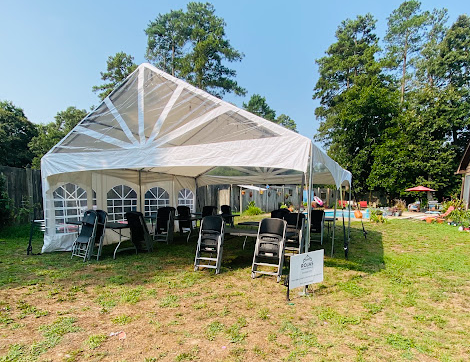 White frame party tent set up in a backyard with tables and chairs